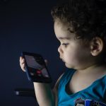 boy in blue tank top holding smartphone