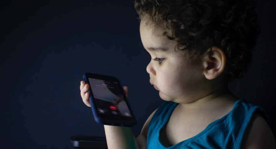 boy in blue tank top holding smartphone